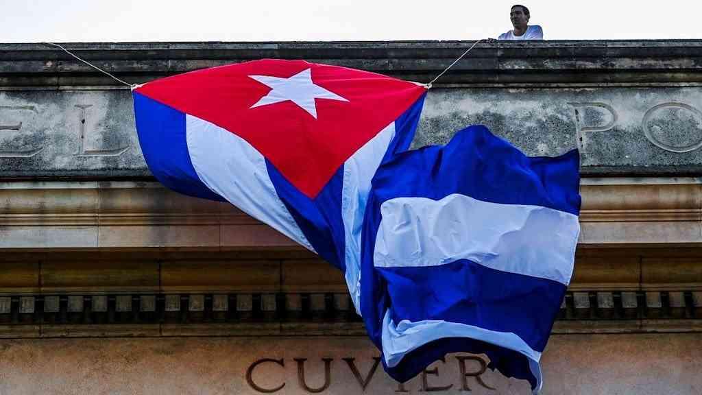 Cuba critica EUA por divulgar notícias falsas sobre luta na Ucrânia | Um homem amarra uma bandeira cubana no telhado da Universidade de Havana após os resultados da votação do projeto de resolução para acabar com o embargo dos EUA