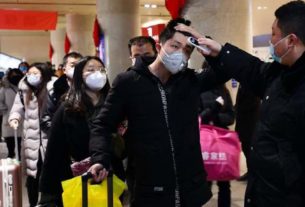 Funcionário checa a temperatura corporal de passageiros na estação de trem de Jinan, no oeste da China