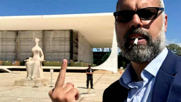 O blogueiro bolsonarista Allan dos Santos deixa o gesto pornográfico de recado para o STF, após sair do país e não deixar o endereço