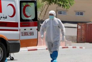 Agente de saúde palestino caminha em direção a ambulância após morte de idoso por covid-19 em Gaza